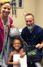 dentist and medical assistant smiling with young girl in dental chair
